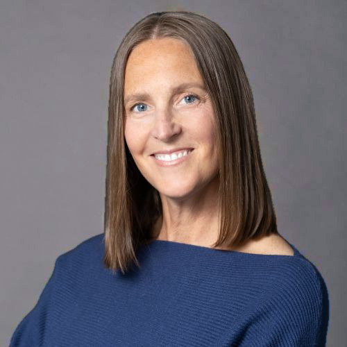 Headshot of a smiling woman with shoulder-length brown hair, wearing a blue textured top.